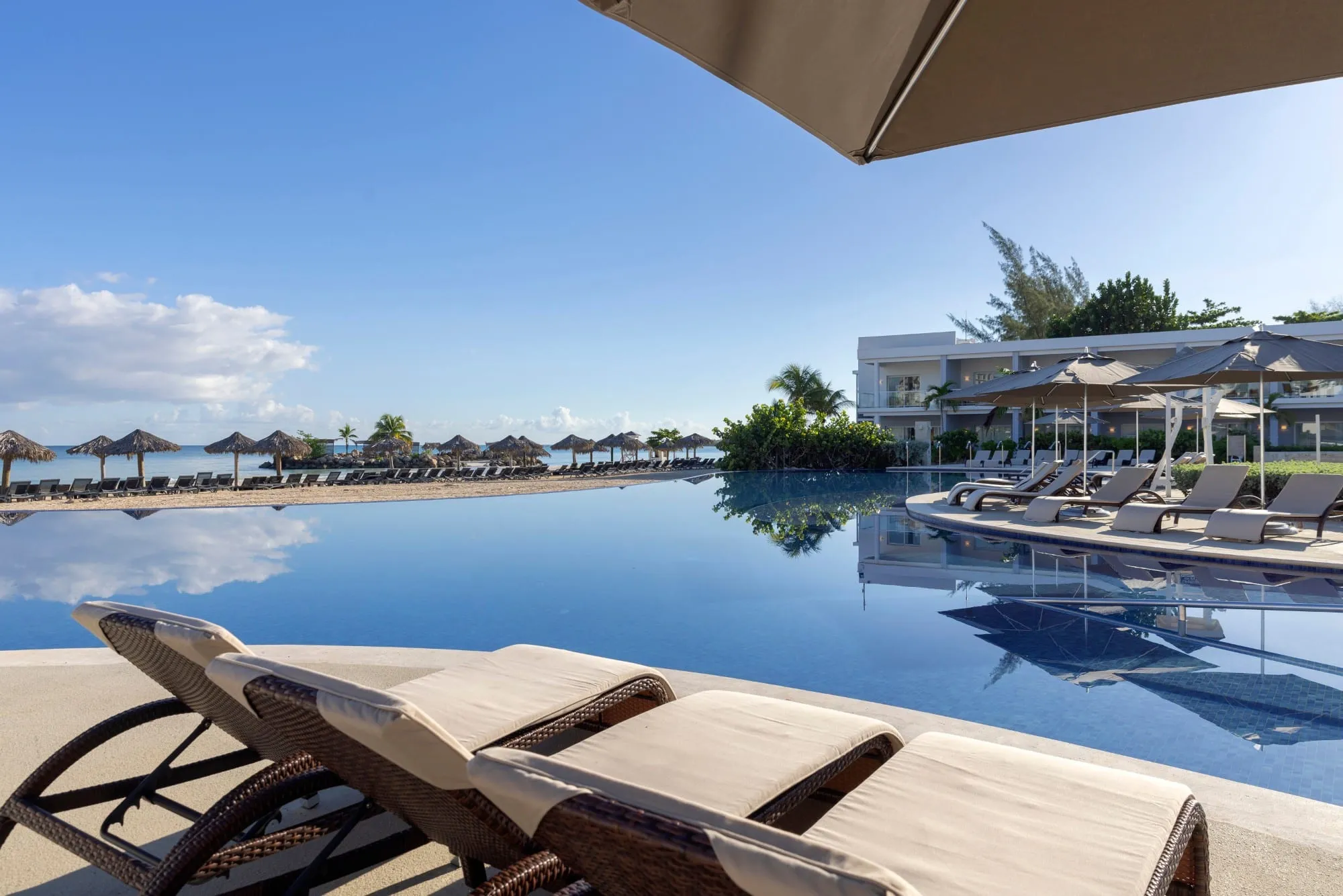 Loungers beside an infinity pool that runs out toward a beach lined with thatched umbrellas
